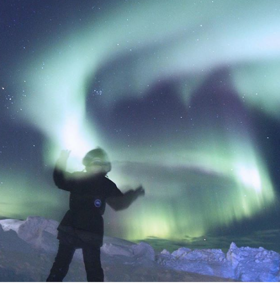 A figure standing below the Aurora, with snow in the background