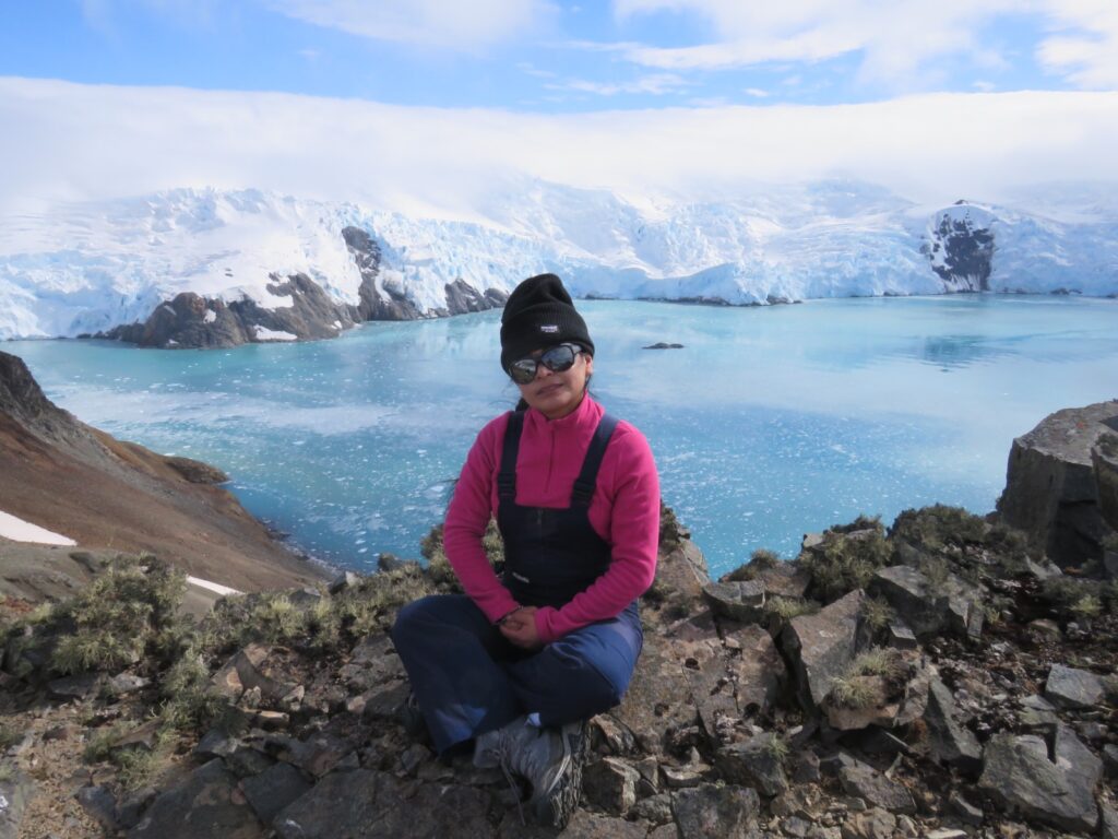 Evelyng is sitting on rocks in front of a glacier. Picture taken during her fieldwork on King George Island, Antarctica, in a glacial environment where she conducted research on cryospheric processes and permafrost.