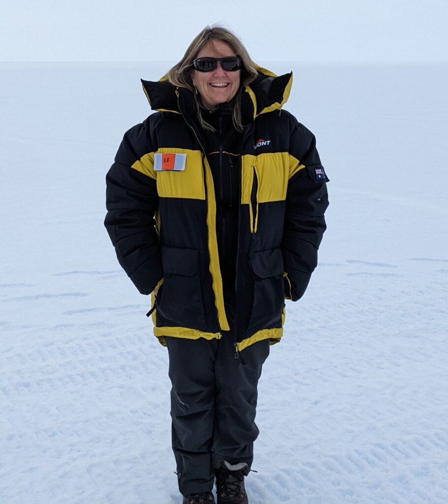 Barbara, in black-and-yellow polar gear, is on the ice, laughing into the camera.